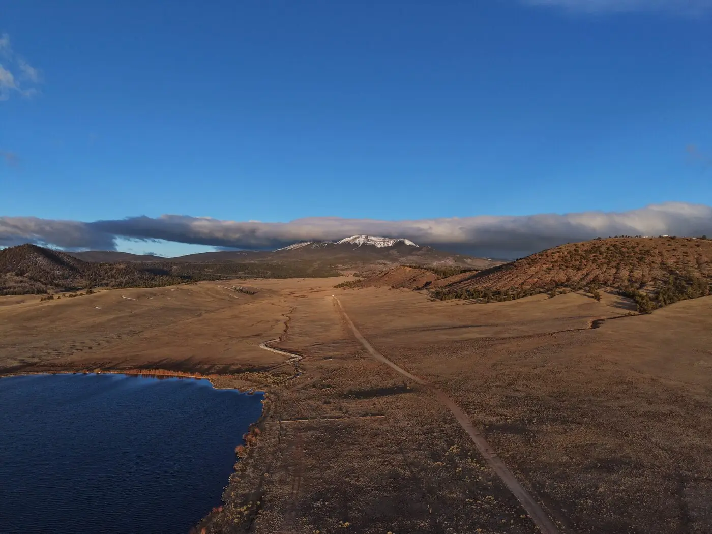 Aerial landscape photography of a snow-capped Colorado mountain range above open plains and a lake