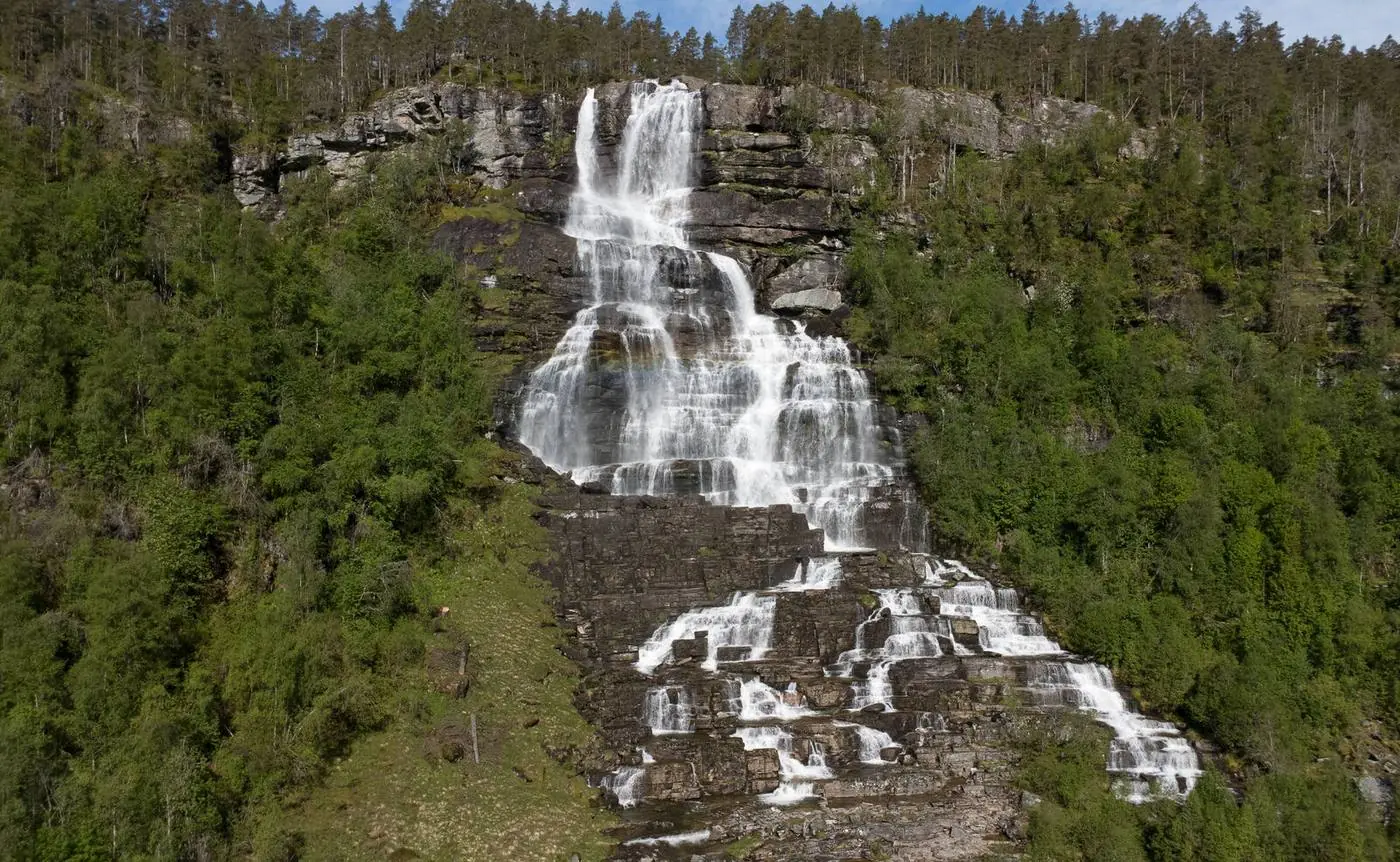 Aerial landscape photography of a tiered waterfall on a forested cliff in Norway