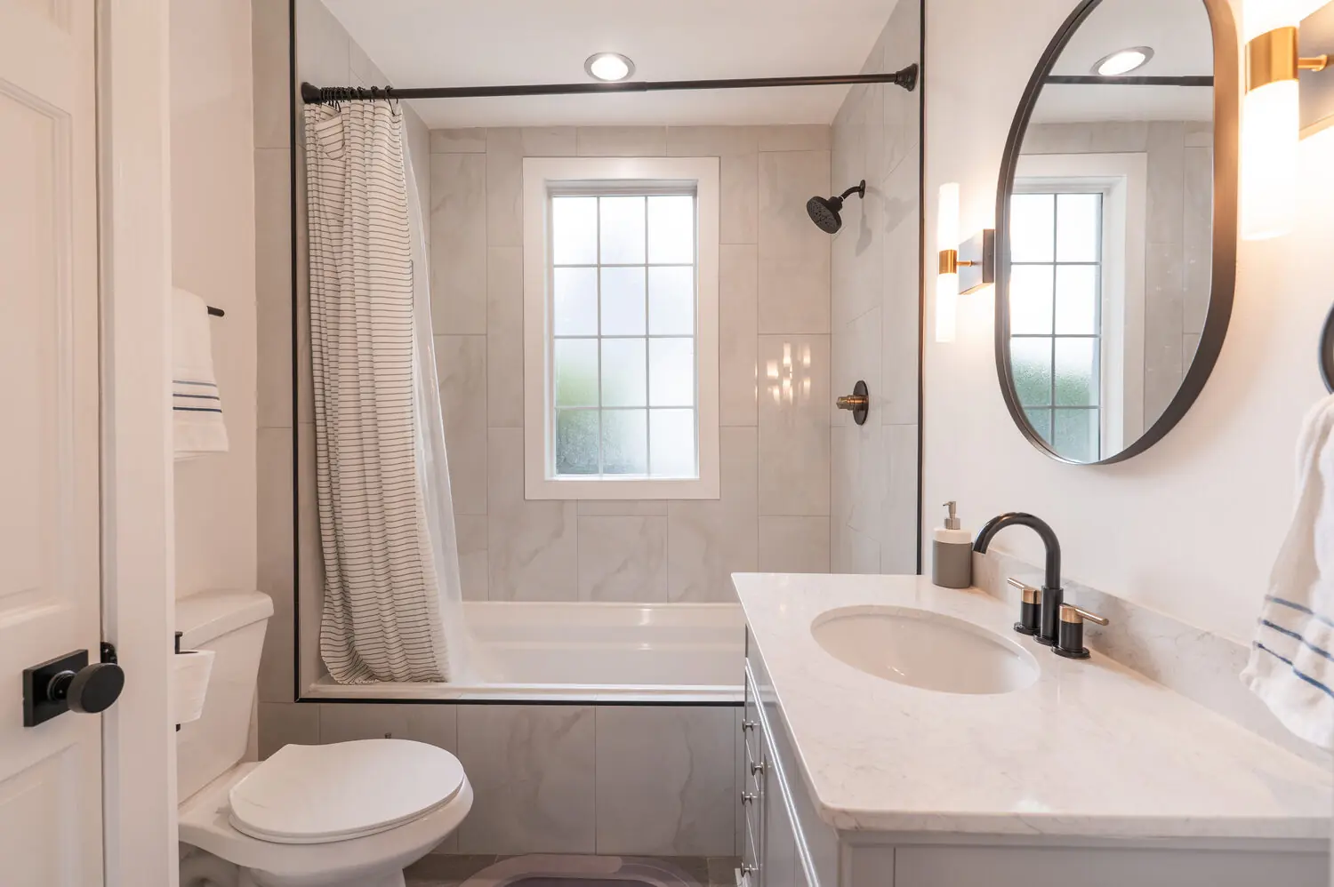 Secondary bathroom with tiled tub and shower, round mirror, and stone vanity, greater Richmond VA