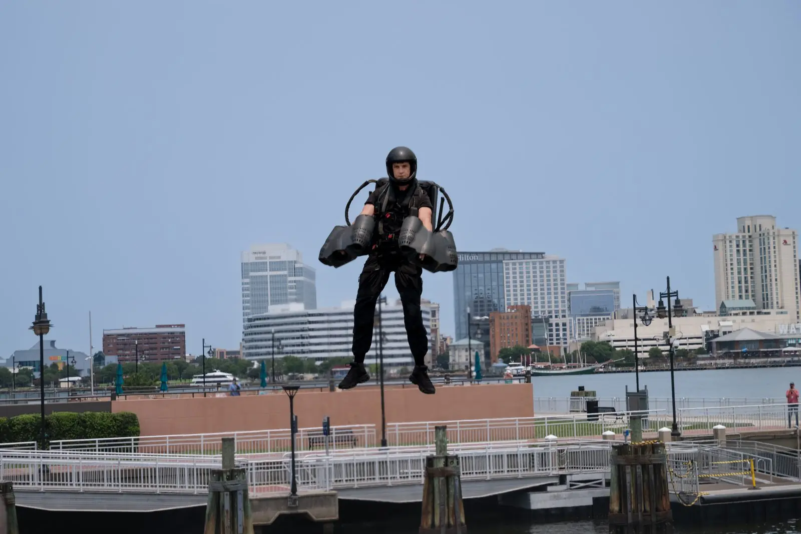 Sports and action photography of a jetpack pilot in flight over a city waterfront, shot on a Nikon Z8