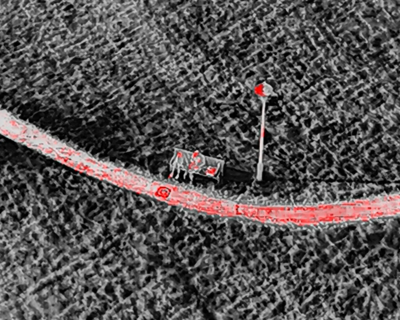 Thermal drone image of a person on a park path with a bench and lamppost, isotherm palette highlighting warm surfaces